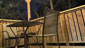An outdoor deck with wooden railings, a metal table and chairs, and string lights. - Rustic Romantic Bayberry Cottage at Autumn Ridge (Lexington)