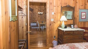 Una habitación con paneles de madera, una cama, un aparador y una puerta abierta que da a un comedor.