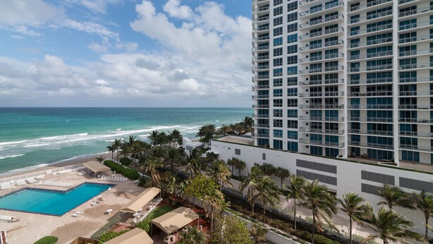 A high-rise hotel with a pool area, palm trees, and a view of the ocean. - On The Beach !!!  2 Minutes to Exquisite Dinning and Shopping (Hallendale Beach)
