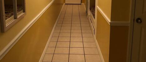 A narrow hallway with yellow walls, a tiled floor, and a door at the end.