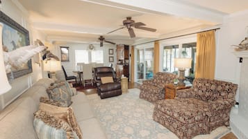 A spacious living room with a ceiling fan, a fireplace, and a large window with curtains.