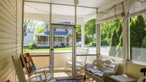 Ein überdachter Balkon mit Korbmöbeln, einem Deckenventilator und Blick auf ein Haus und eine Straße.