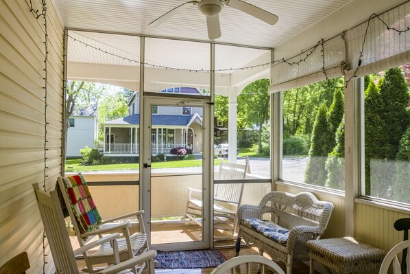 A covered porch with wicker furniture, a ceiling fan, and a view of a house and street.