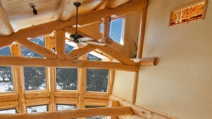 Interior espaçoso de uma cabana, com escada de madeira, janelas amplas e um espaço de estar acolhedor.