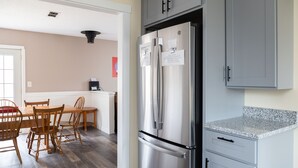Een keuken met een roestvrijstalen koelkast, een houten eettafel en stoelen.
