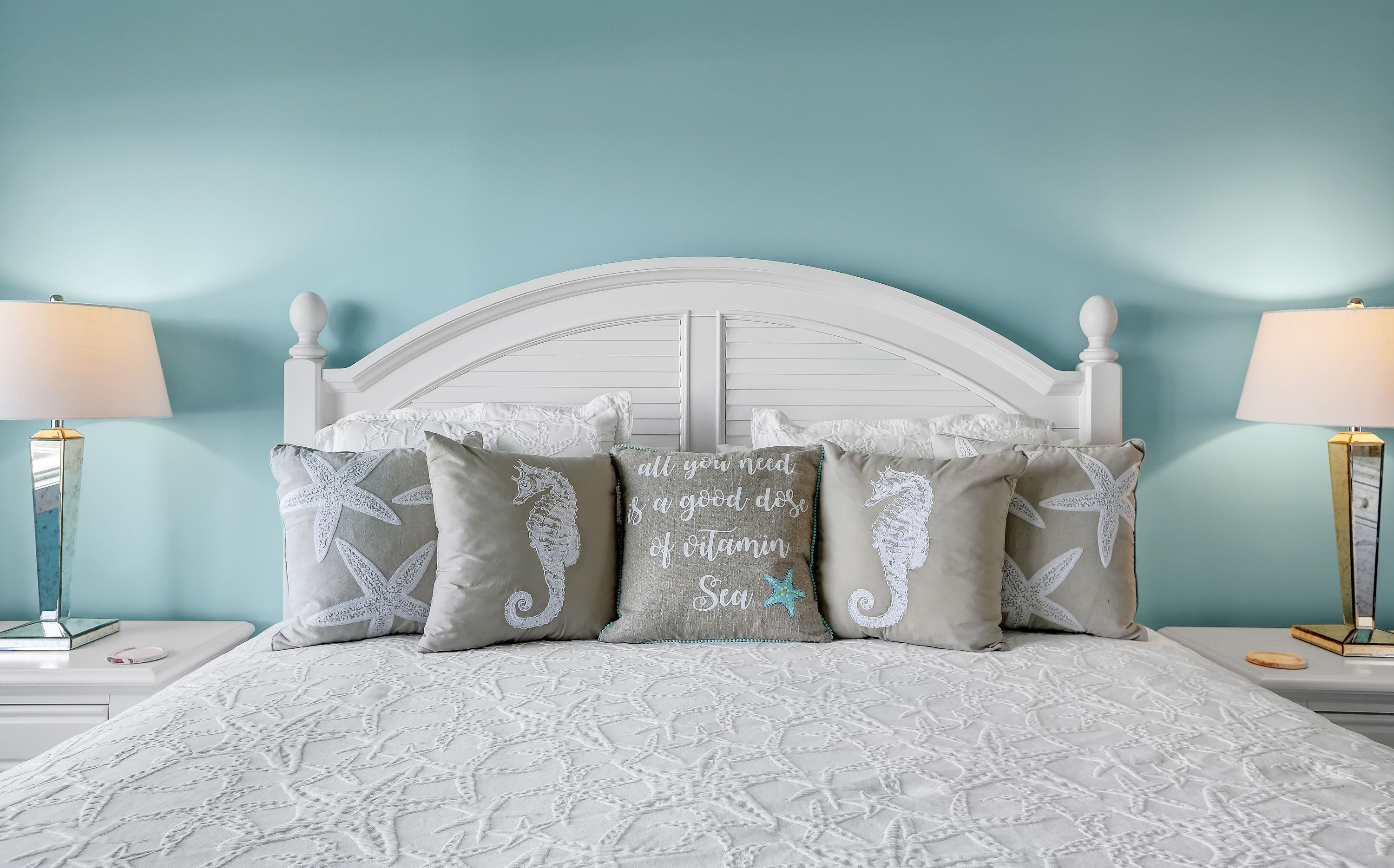 A bed with a white headboard and multiple pillows, including one with a sea-themed design.
