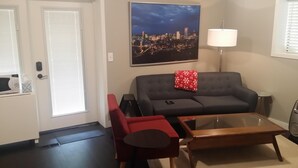 Ein Wohnzimmer mit grauem Sofa, einem roten Sessel, einem Glastisch und einem Stadtbild an der Wand.