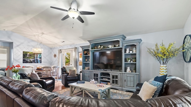 A living room with a brown leather sofa, a wooden coffee table, a television on a blue cabinet, and a ceiling fan.