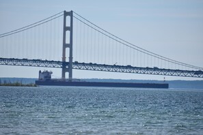 Eine große Hängebrücke überspannt ein Gewässer, im Vordergrund ein Frachtschiff.