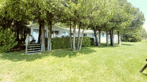 Une maison blanche dotée d’un porche abrité, entourée d’une pelouse bien entretenue et d’arbres.