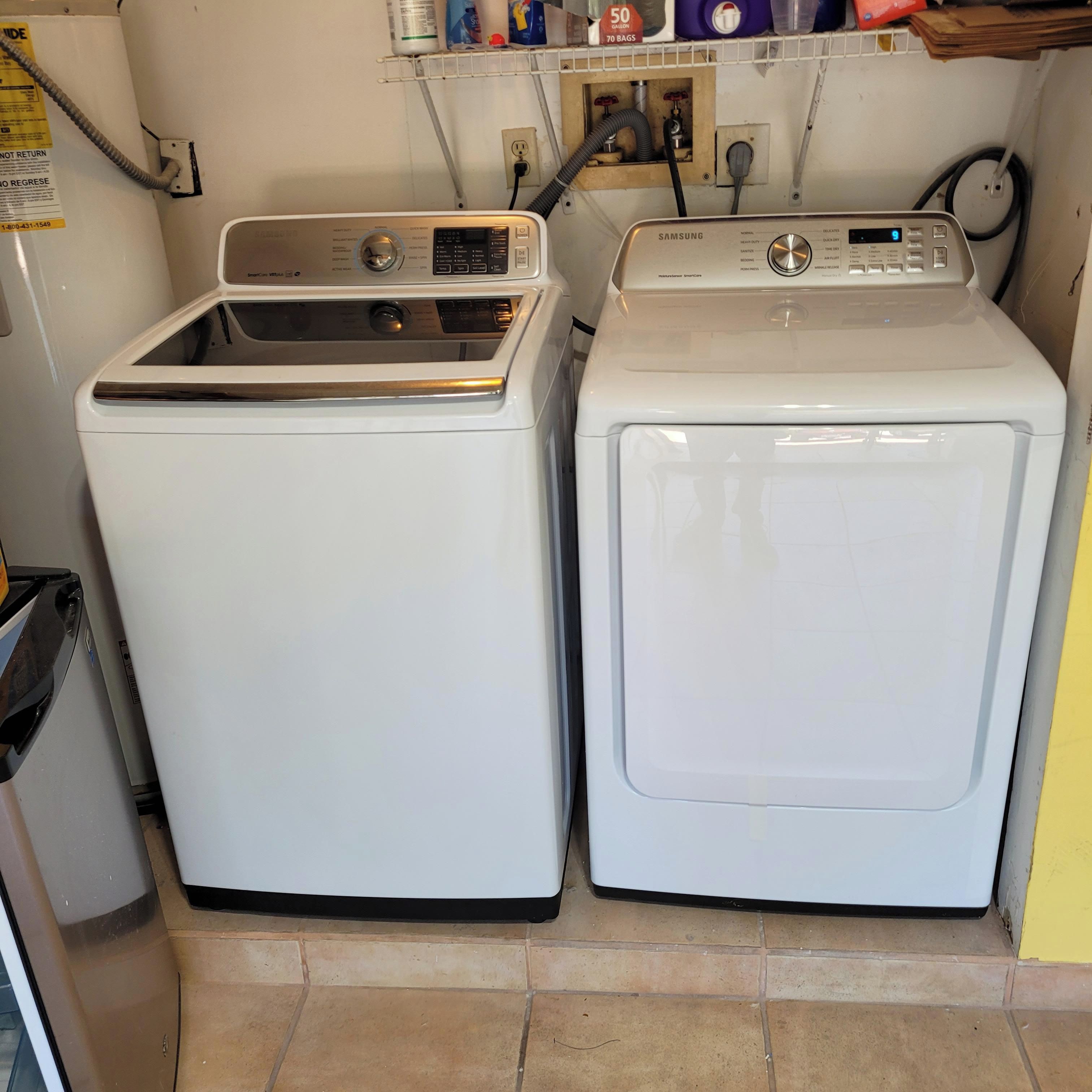 Two stacked washing machines in a laundry area with a utility wall, a water heater, and a power outlet.