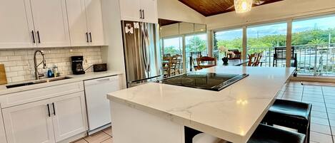 A modern kitchen with white cabinetry, a large island, and a view of the outdoors.