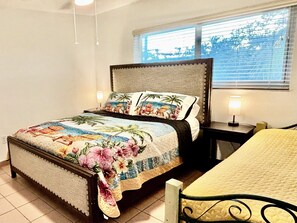 A bed with a floral bedspread, a bedside table with a lamp, and a window with blinds. - Key Largo Oceanfront Villa and Marina (Key Largo)