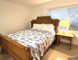 Une chambre à coucher avec un lit en bois, une table de chevet avec une lampe et une fenêtre avec des stores.
