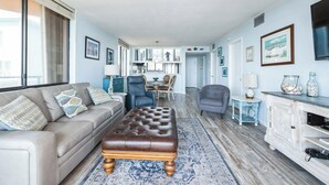 Un salon spacieux avec un canapé beige, un pouf en cuir marron, un tapis à motifs bleus et un meuble blanc agrémenté d’objets décoratifs.