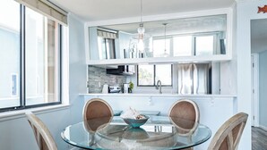 Une cuisine moderne avec une table à manger en verre, deux chaises et un luminaire suspendu.