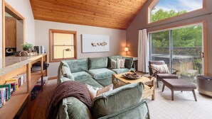 A cozy living room with a green sectional sofa, a wooden coffee table, and a large window offering a view of the outdoors.