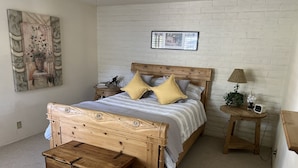 Un dormitorio con una cama de madera, una mesita de noche, una lámpara, un cuadro enmarco y un baúl de madera.