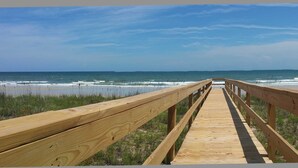 Une promenade en bois qui mène à une plage d’où l’on a une vue dégagée sur l’océan.