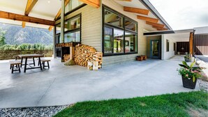 A modern house with large windows, a stone fireplace, and a patio with a table and benches. - 5-Star Lodge \ Groups Welcome  \ 1 Mile from Downtown (Leavenworth)