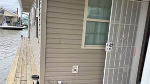 A wooden dock with a house beside it, a window, and a door with a metal grill. - Houseboat ( 2br, 1ba) • Venice Marina (Venice)
