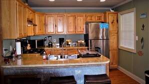 A kitchen with wooden cabinets, stainless steel appliances, a marble countertop, and a small island with stools. - Houseboat ( 2br, 1ba) • Venice Marina (Venice)