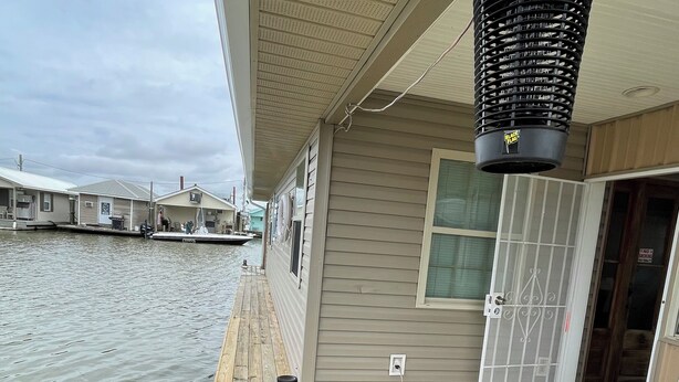 A wooden deck with a water view, a covered area with a ceiling fan, and a door with a metal gate. - Houseboat ( 2br, 1ba) • Venice Marina (Venice)