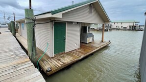 A waterfront cabin with a green door, a small deck, and a dock extending into the water. - Houseboat ( 2br, 1ba) • Venice Marina (Venice)