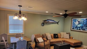 A living room with a sectional sofa, a dining table with chairs, a ceiling fan, and a fish wall decoration. - Houseboat ( 2br, 1ba) • Venice Marina (Venice)