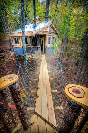Un puente colgante de madera que lleva a una cabaña en un bosque.
