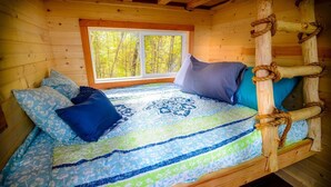 Un dormitorio de cabaña de madera con una cama, almohadas y un ventanal con vistas a árboles.