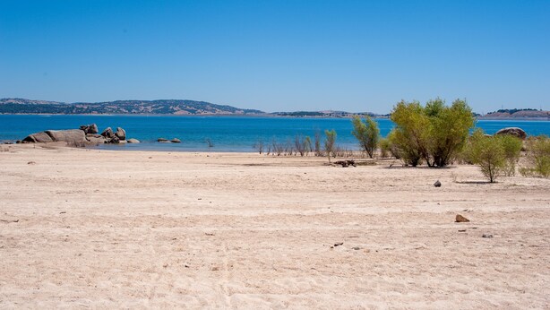 A beach with clear blue water, sandy shore, and sparse vegetation. - Lake front getaway! Casita d’Amore (Granite Bay)