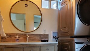 A bathroom with a wooden vanity, a round mirror, a washing machine, and a dryer. - Lake front getaway! Casita d’Amore (Granite Bay)