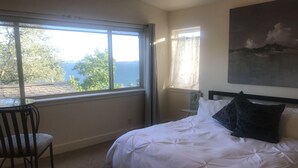 A bedroom with a bed, a chair, a window with a view of trees and a body of water, and a painting on the wall. - Lake front getaway! Casita d’Amore (Granite Bay)