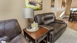 Ein Wohnzimmer mit braunem Ledersofa, einem Holztisch mit Lampe und einem Bild an der Wand.