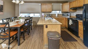 Eine moderne Küche mit Holzausbau, einer zentralen Kochinsel, einem schwarzen Kühlschrank und einem Essbereich mit Stühlen und Tisch.