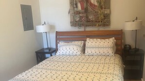 Een slaapkamer met een houten bed, beddengoed met een patroon, een aan de muur hangend kunstwerk, bedlampen en een klein nachtkastje.