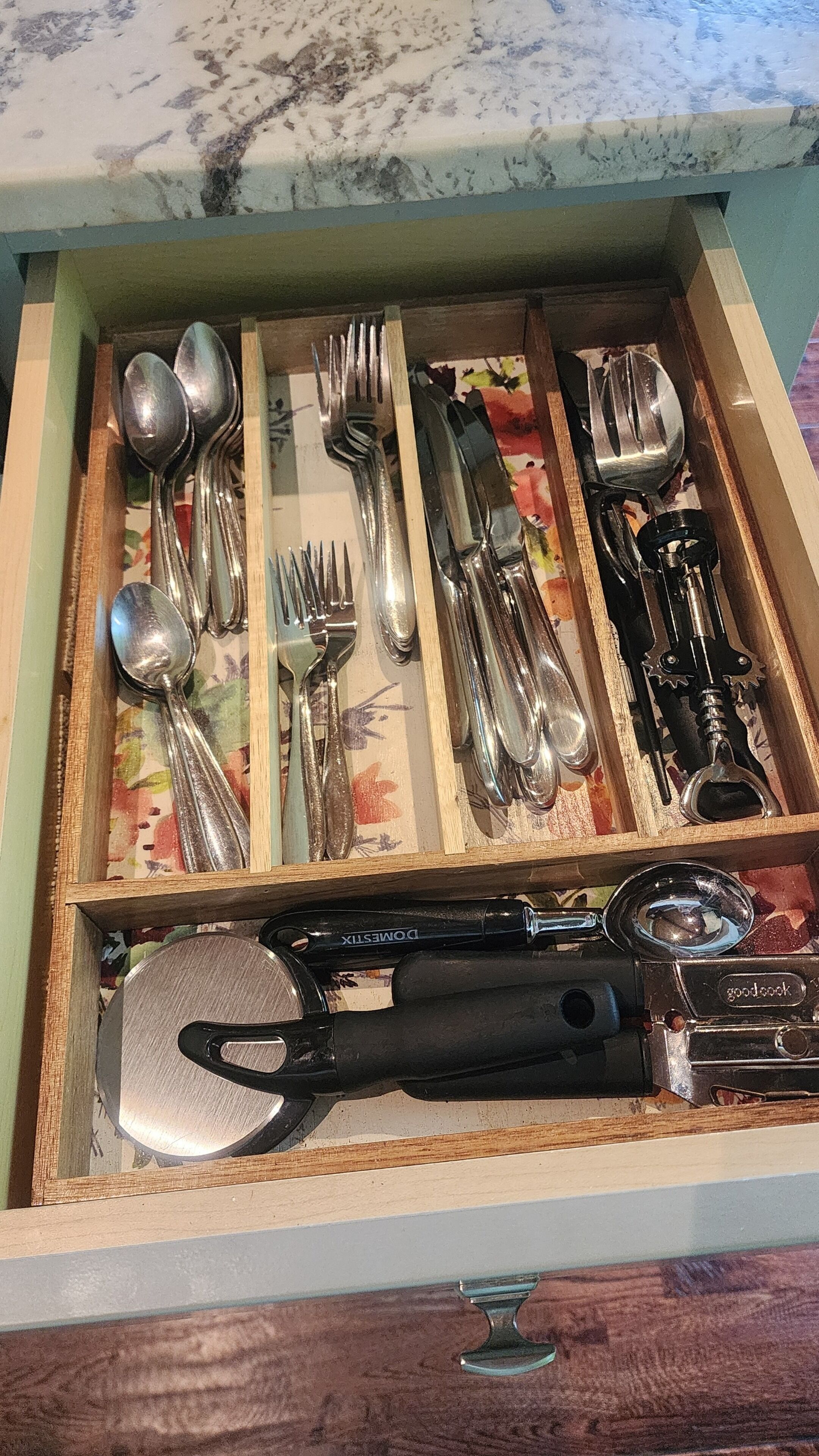 A drawer with various kitchen utensils including spoons, forks, knives, and a can opener.