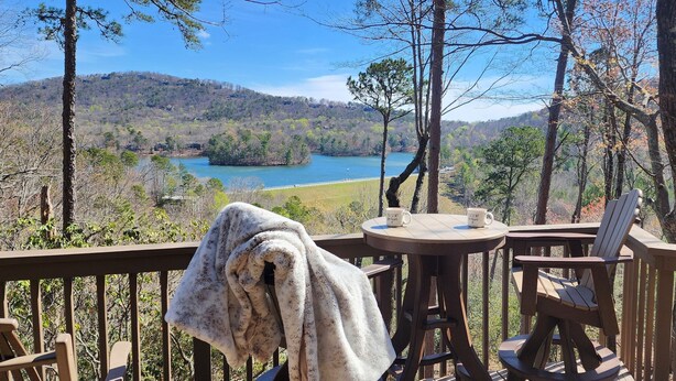 A balcony with a view of a lake, a table with chairs, and a towel draped over a chair. - Couples Retreat with Hot Tub, Lake & Mountain Views in Big Canoe Luxury Resort (Jasper)