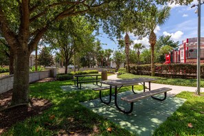 Relax in the serene park area surrounded by lush greenery and mature trees, with picnic tables and a beautifully maintained landscape.