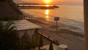 Vista da praia com um pôr do sol, uma estrutura de telhado de palha e uma placa com a inscrição 'TUI GLOBE'.