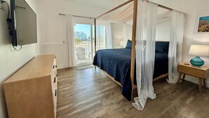 Un dormitorio con cama con dosel, ventilador de techo, televisor montado en la pared y vistas al exterior a través de una puerta corrediza.