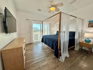 A bedroom with a four-poster bed, a ceiling fan, a TV mounted on the wall, and a view of the outside through a sliding door. - #1 Reviewed Home on Navarre Beach Forever Views 33' Pool Outdoor Bar/TVs Hot Tub (Navarre)