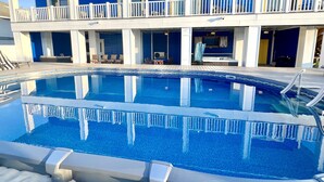 Una piscina con cubierta blanca y un edificio al fondo con paredes azules y barandillas blancas.