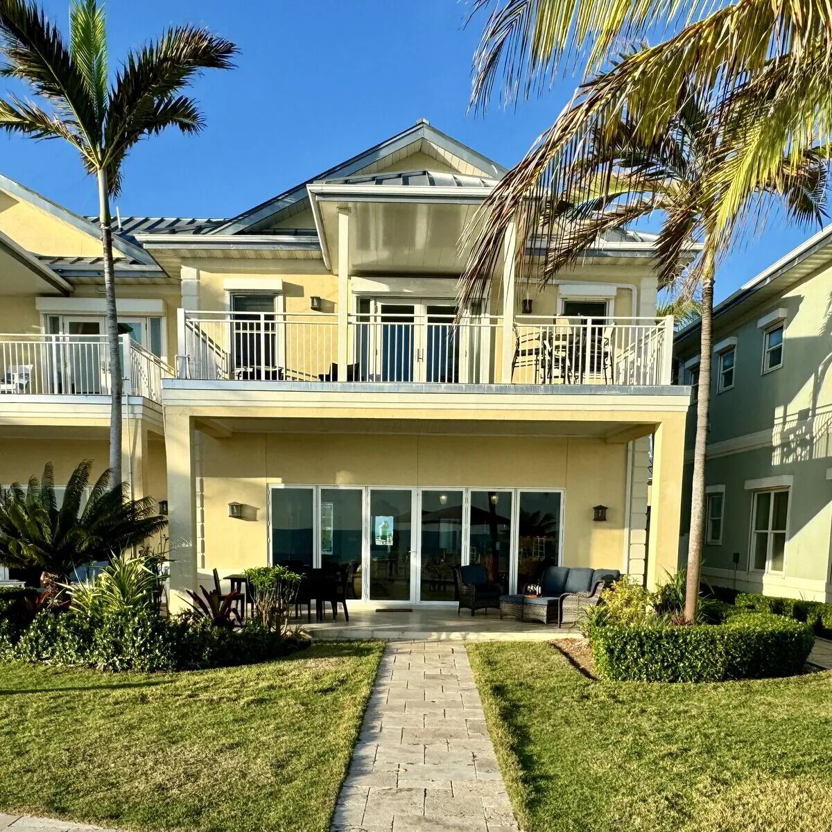 A two-story building with a balcony, a patio with outdoor furniture, and a well-maintained lawn.