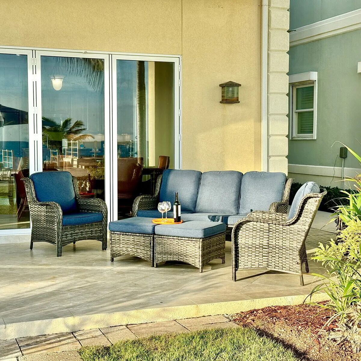 A patio area with wicker furniture, including a sofa and chairs, and a small table with a bottle and glasses.