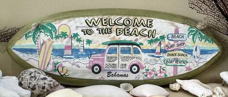 A beach-themed welcome sign with amenities like a beach, surf shop, snack shack, and boat rental.