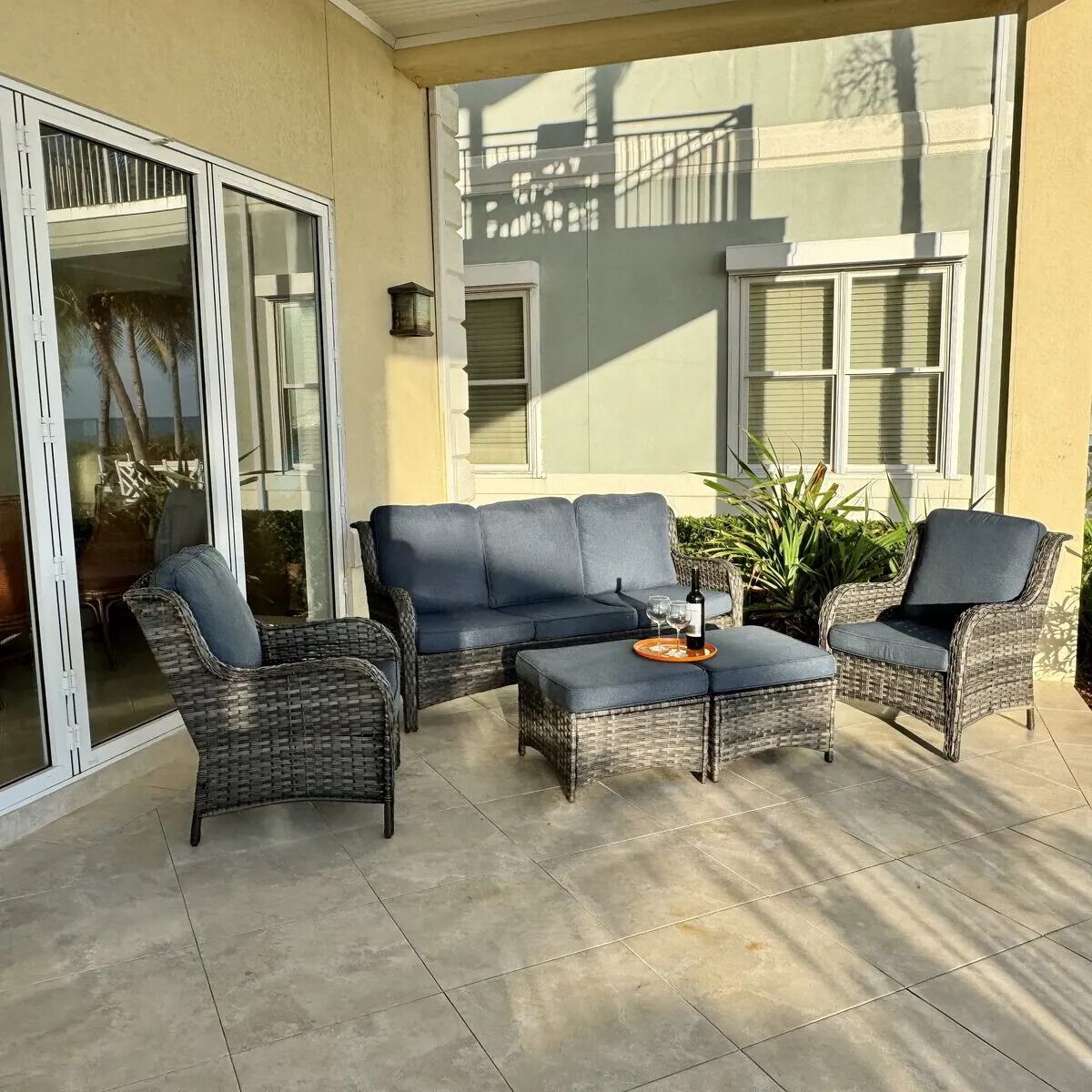 A covered patio area with wicker furniture, including a sofa and two armchairs, and a small table with a bottle and glasses.