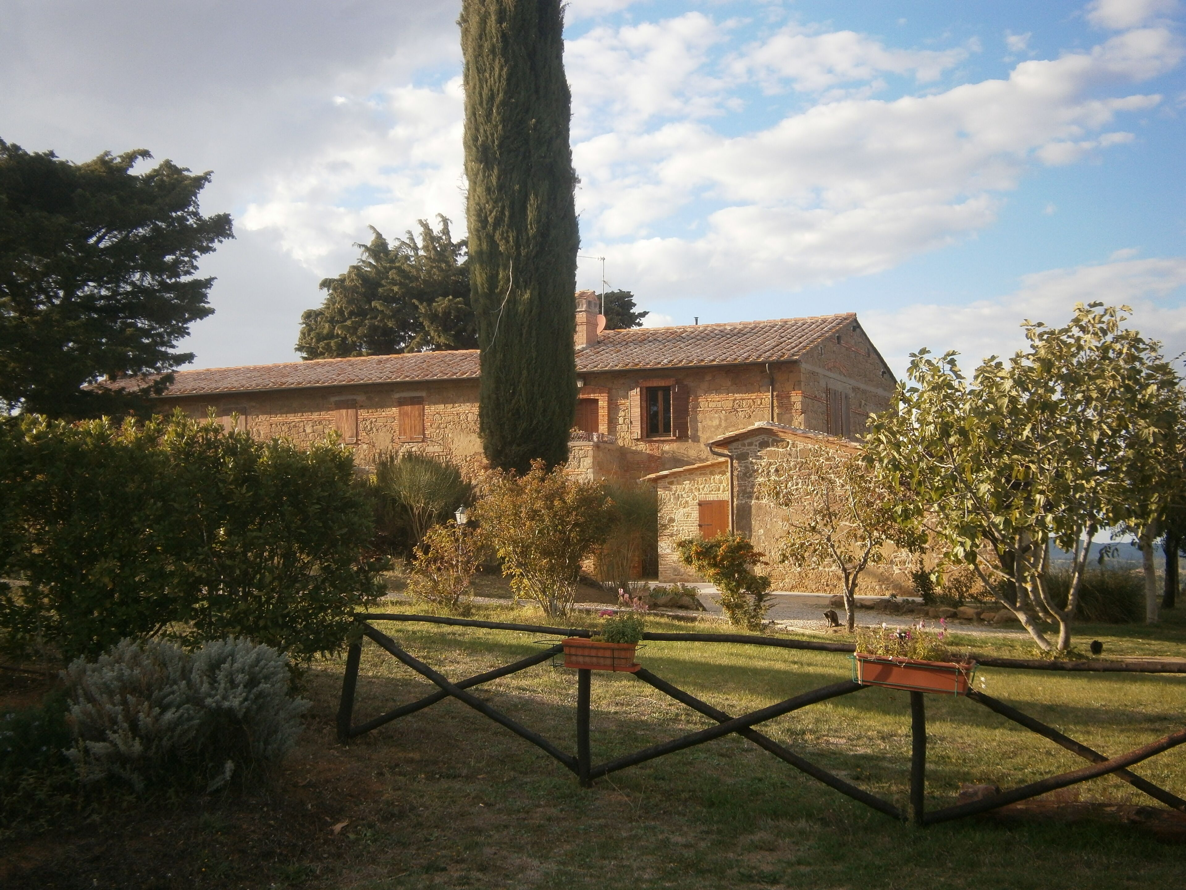 A stone building with a tiled roof, surrounded by a fenced garden with potted plants.