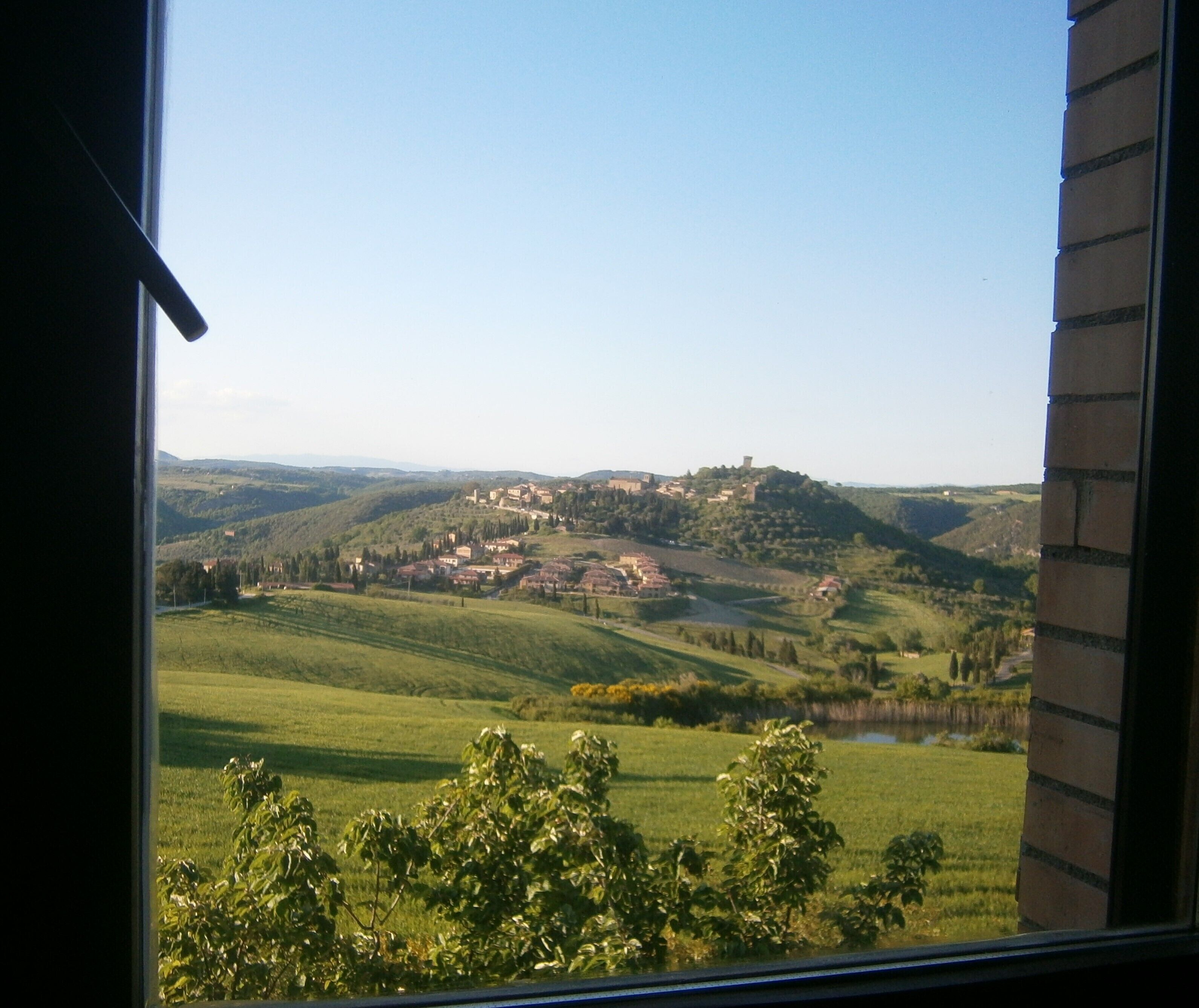 A view of a rural landscape with rolling hills, a small village, and a body of water.